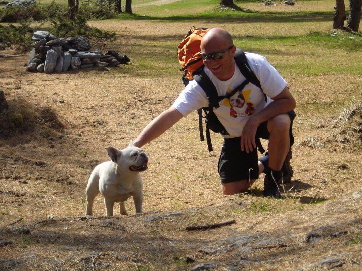 A smiling man on a field smiling and caressing a white French Bulldog