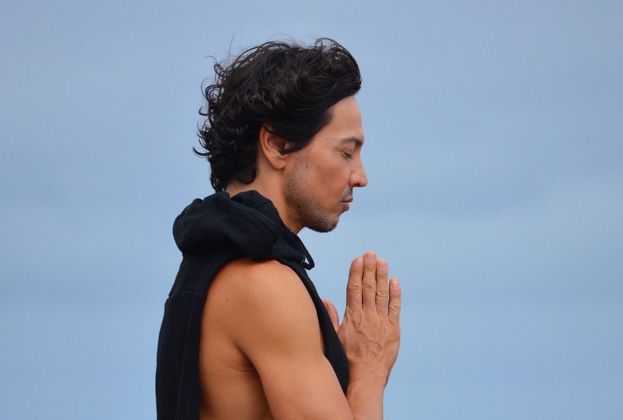 Young black haired man joining hands in prayer on a blue sky background