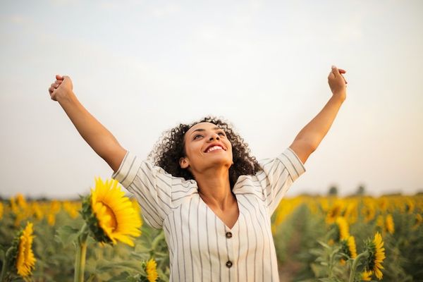 Woman smiles with raised open arms looking at the sky in a sunflower field